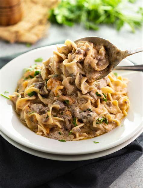 A White Plate Filled With Egg Noodles In A Stroganoff Sauce With Ground Beef And A  Beef