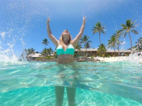 Low Angle Smiling Young Woman Splashing Glassy Ocean Water With Her