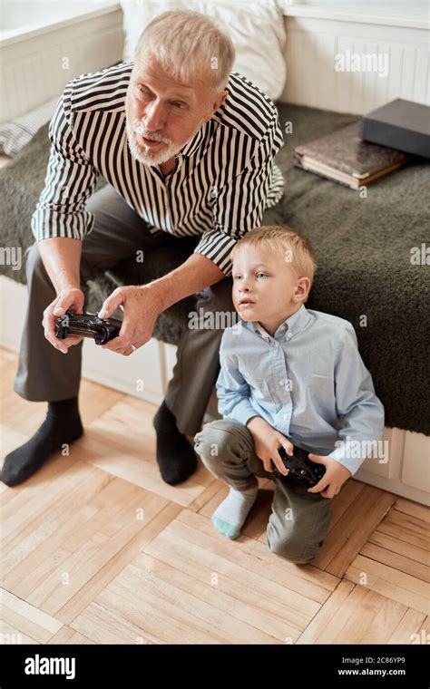 Grandfather And Grandson Playing Video Game With Joysticks In Bed Room