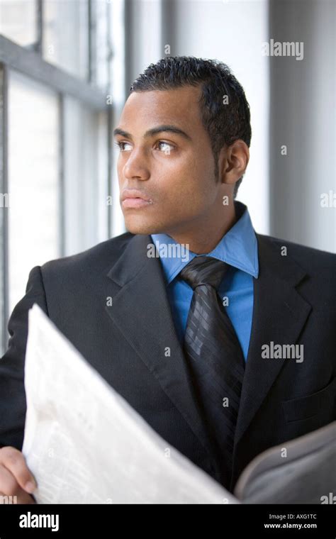 A Young Business Man Reading A Newspaper By A Window Wearing A Suit And