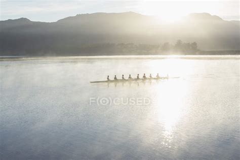 Rowing team rowing boat on still lake — bonding, health - Stock Photo | #199749866