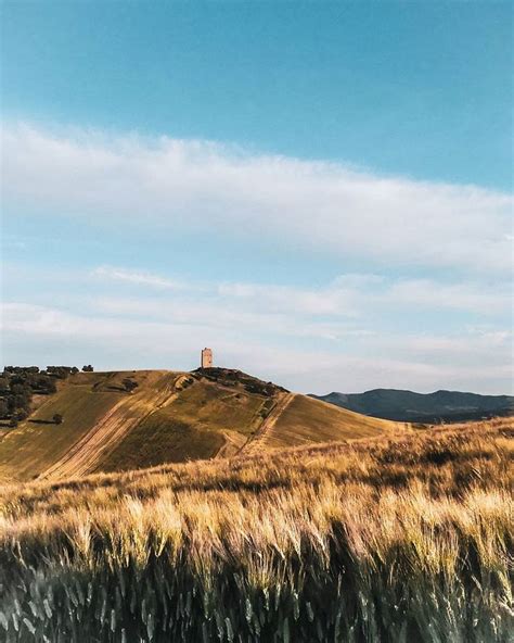 A Grassy Hill With A Small Tower On Top In The Distance And Blue Sky Above