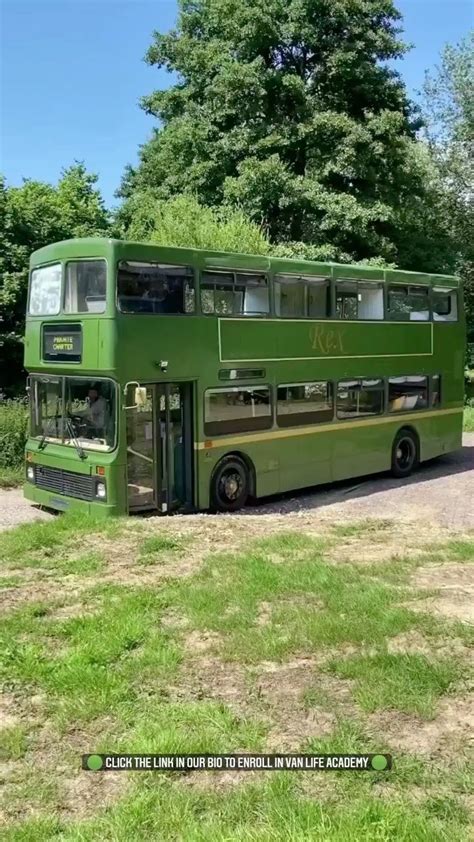 a green double decker bus parked on the side of a road in front of some trees