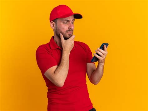 Dudoso Joven Repartidor Cauc Sico En Uniforme Rojo Y Gorra Manteniendo