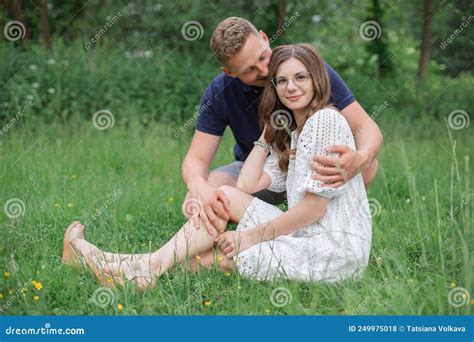 Affectionate Young Couple Sitting On Grass In Park Kissing Young Man