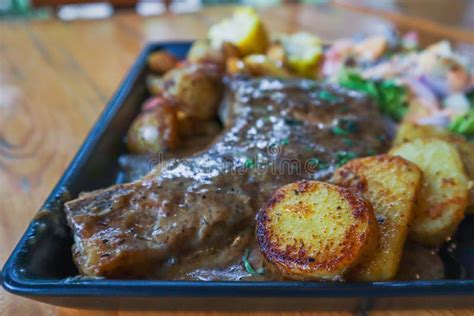 Grilled Beef Steak With Gravy Is Served With A Fruit And Vegetable Salad Inside A Black Ceramic