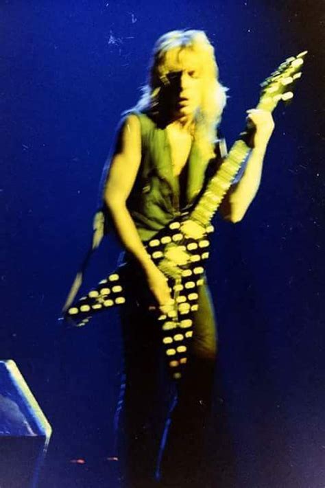 A Man With Long White Hair Holding A Guitar In His Right Hand While Standing On Stage