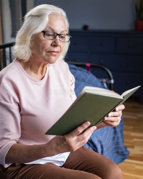 Calm Senior Woman Reading A Book While Sitting In The Living Room Stock