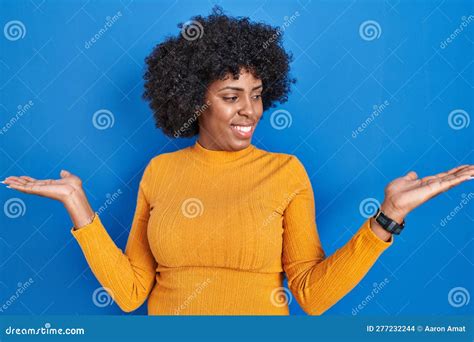 Black Woman With Curly Hair Standing Over Blue Background Smiling Showing Both Hands Open Palms