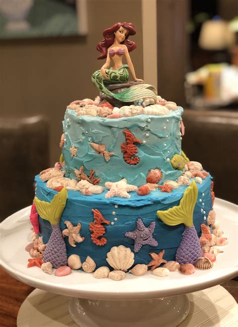 There Is A Cake Decorated With Mermaids And Seashells On The Top Tier