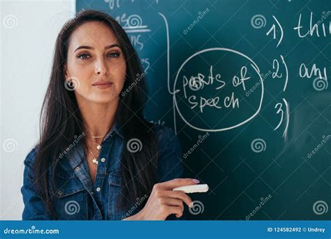 Portrait Of Young Female Teacher Against Chalkboard In Class Stock