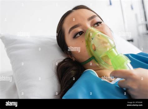 Sick Asian Woman Lying In Oxygen Mask And Looking Away In Hospital Ward