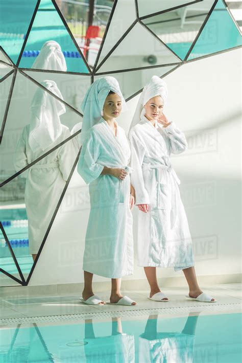 Beautiful Young Women In Bathrobes Standing Next To Swimming Pool At