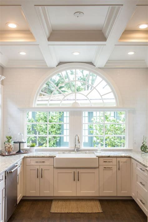 A Kitchen With An Arched Window And White Cabinets