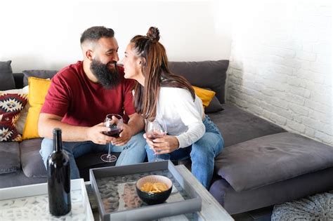 Una pareja sentada en el sofá de casa mirándose sonriendo y a punto de