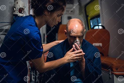 Nurse In Uniform Holds Oxygen Mask On Man Sitting In Blanket Stock