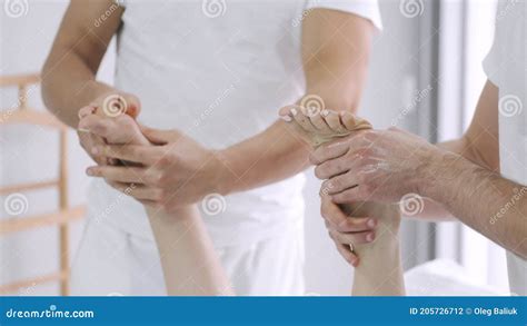 Two Male Massage Therapists Doing Massage Of The Legs Of A Young Girl