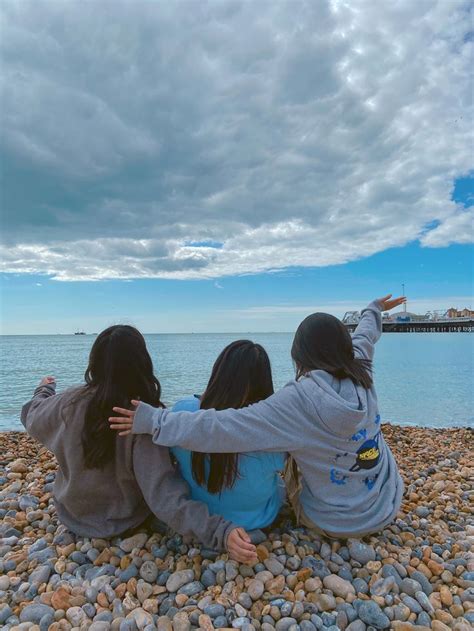 Three Girls Sitting On The Beach Looking Out At The Water And Clouds In