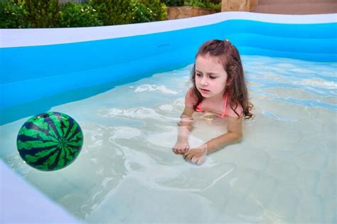 Adorable niña pequeña juega con una pelota flotante mientras nada en la