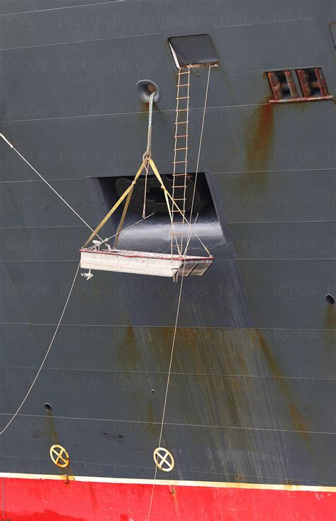 "Primitive Little Boat Hanging On The Side Of A Huge Ship" by Stocksy