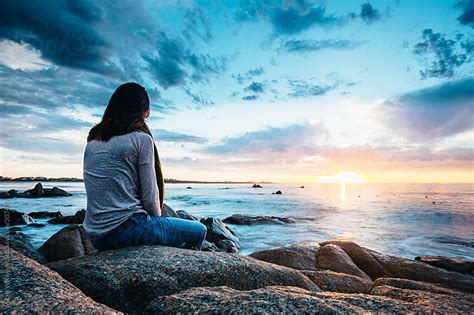 woman sitting on a rock enjoying a beautiful sunset view over the sea by Micky Wiswedel ...