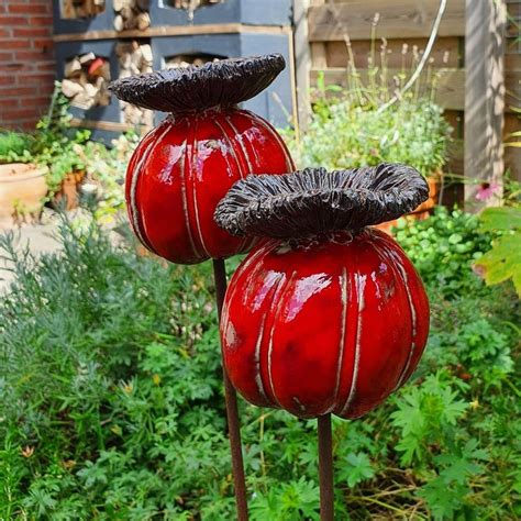 Two Red Vases Sitting On Top Of Metal Poles In Front Of Some Bushes And