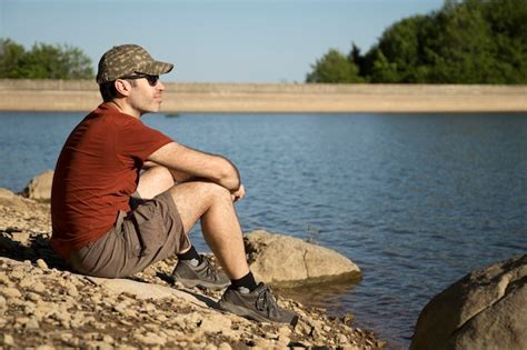 Premium Photo Side View Of Man Wearing Cap Sitting On Rock By River