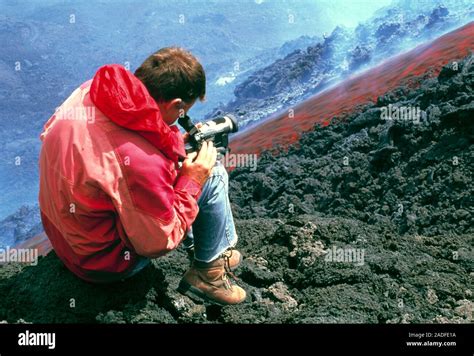 Volcanologist with a camcorder by a lava flow on the volcano Mount Etna. Lava (molten rock ...