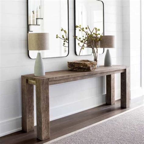 Two Mirrors On The Wall Above A Wooden Table With Vases And Flowers In