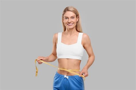 Premium Photo Slim Woman Measuring Waist With Tape On Grey Background