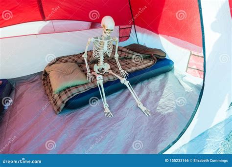 Skeleton Sitting On Blow Up Mattress In A Tent While Camping Stock