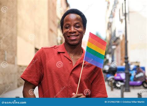 Gay Black Man In A Red Shirt Is Holding A Rainbow Flag And Smiling At