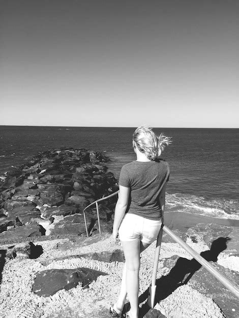 Premium Photo Rear View Of Woman Standing At Rocky Beach Against Clear Sky