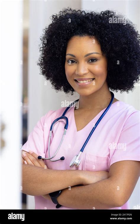 Biracial Nurse Standing With Arms Crossed Wearing Scrubs At Home She