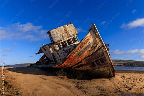 Historic Wooden Fishing Boat Wreck On Sandy Beach In Sun And Blue Sky