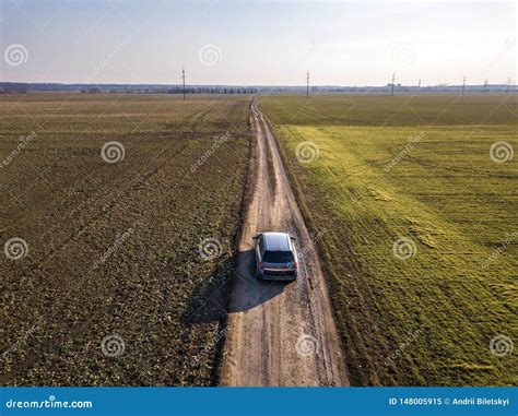 Aerial View Of Car Driving By Straight Ground Road Through Green Fields