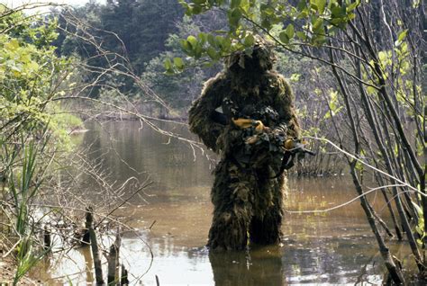 A Marine sniper team member wearing a camouflage ghillie suit crosses a ...