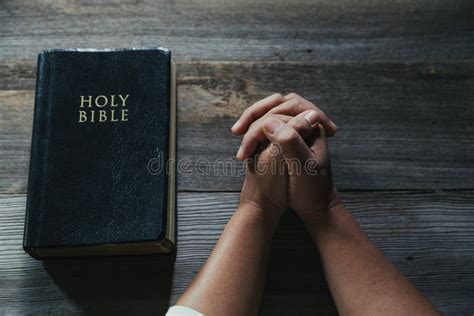 Hands Folded In Prayer On A Holy Bible In Church Concept For Faith