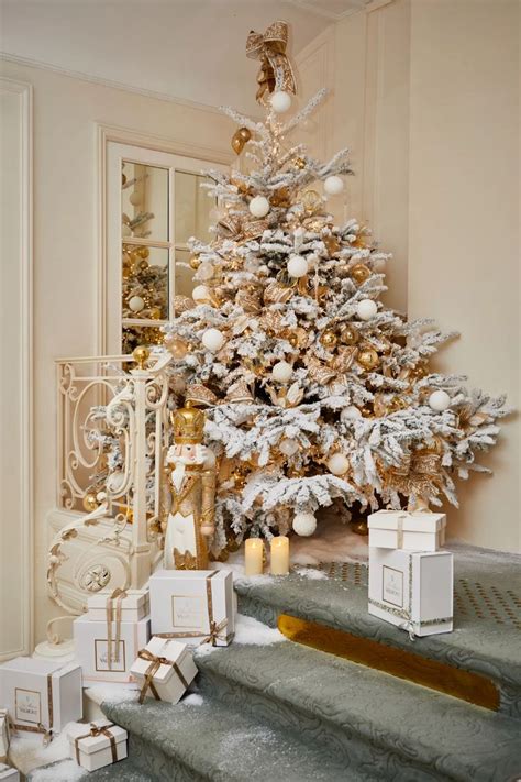 A White Christmas Tree With Gold Ornaments And Presents On The Stairs