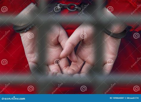 Hands Of The Girl In Handcuffs Behind The Bars Of The Prison Stock