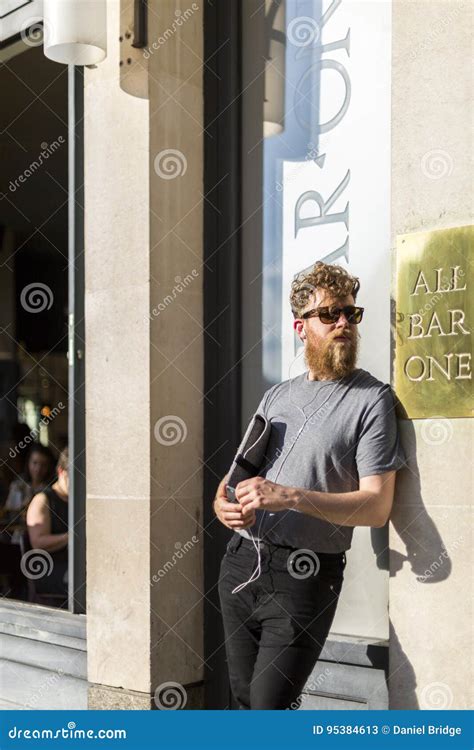 Hipster Man Leans Against Wall On London Street Holding A Laptop