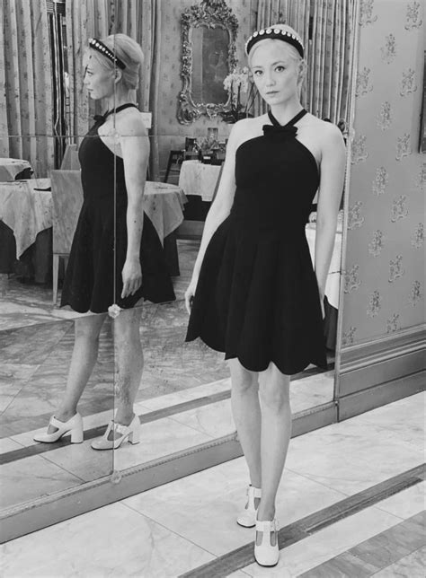 a woman standing in front of a mirror wearing a dress and hat with her ...