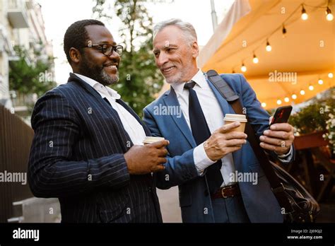 Multiracial Two Men Using Cellphone And Talking While Drinking Coffee