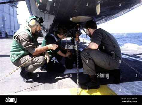 Flight Deck Crewmen Check The Tires Of A Parked Aircraft On The Deck Of