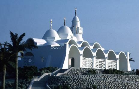 A Large White Building Sitting On Top Of A Lush Green Hillside Next To