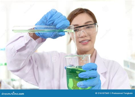 Hands Of Scientist Woman In Lab Coats With Safety Glasses Pouring Chemical From Test Tube Into