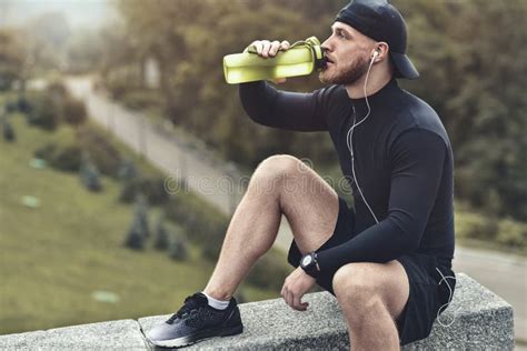 Het Close Up Schoot De Gebaarde Sportieve Mens Neemt Een Rust En Drinkt